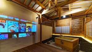 A traditional Japanese onsen with wooden beams, a wooden bath, and a wall with anime posters. - KONJAKUSO Osaka Shinsaibashi "TARUKAISEN" Rooftop SPA (Osaka)