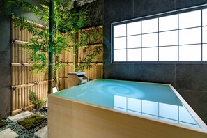 Un área de spa con una bañera grande, plantas de bambú y vistas a través de una ventana.