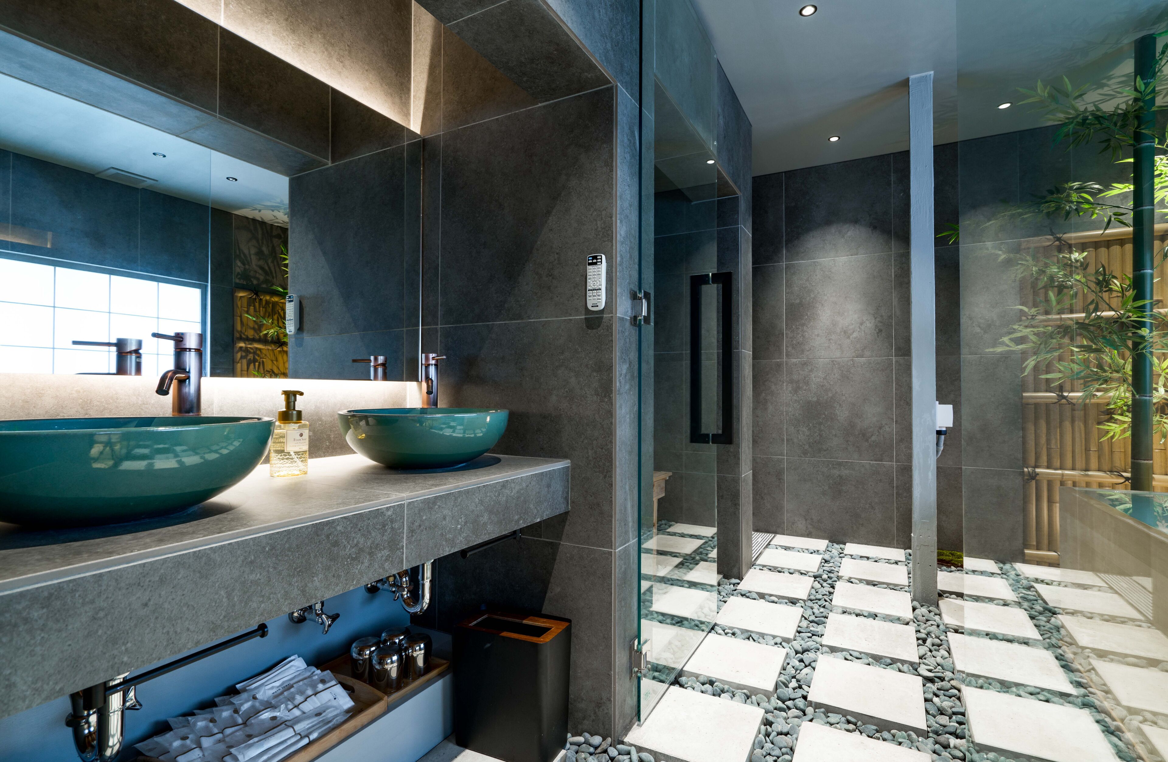 A modern bathroom with a large mirror, two bowls on the counter, a glass shower enclosure, and a checkered floor.