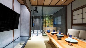 A modern interior with a wooden dining table set for a meal, a flat-screen TV mounted on the wall, and a view of a garden through a glass door. - KONJAKUSO Osaka Bentencho "HIKARIYUYA" Projection Mapping SPA (Osaka)
