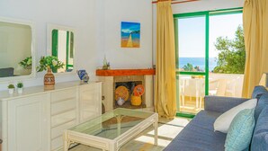 Un salon avec un canapé, une table basse en verre, une cheminée et une vue sur la mer depuis un balcon.