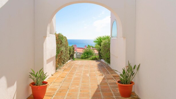 Un étroit sentier mène à un point de vue sur la mer, bordé de murs blancs et de plantes en pot.