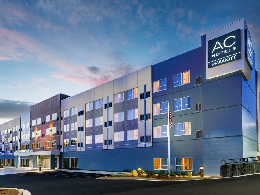 A modern hotel building with multiple floors, a prominent AC Hotels Marriott sign, and a flagpole with an American flag.