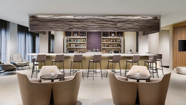 A modern bar area with a central bar counter, seating with round tables, and a variety of bottles on shelves. - AC by Marriott Portland Beaverton (Beaverton)