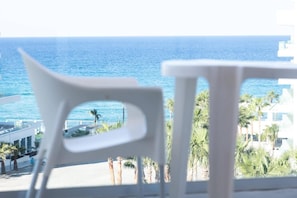 Un balcone con vista sul mare, sedie bianche e palme.
