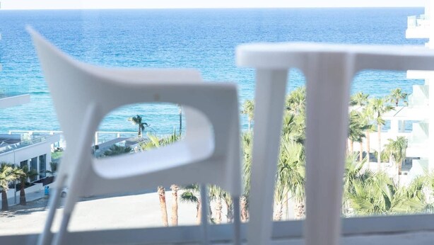 A balcony with a view of the sea, white chairs, and palm trees. - Vrissaki Hotel Apartments (Paralimni)