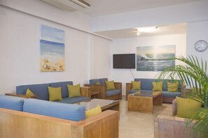 Un hall d’hôtel avec un canapé bleu, des tables basses en bois et un téléviseur fixé au mur.