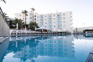 Une piscine avec des chaises longues, un bùtiment blanc doté de balcons et des palmiers.