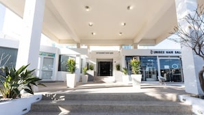 A hotel entrance with steps leading up to the door, potted plants, and a salon across the street. - Vrissaki Hotel Apartments (Paralimni)