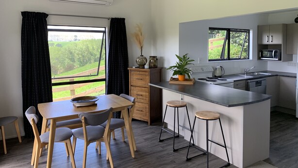 Una cocina moderna con una isla central, sillas de madera, una mesa de comedor y vistas a un paisaje verde a través de amplios ventanales.