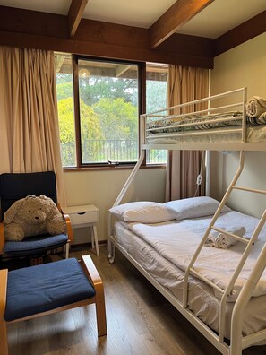 Habitación con literas, un escritorio, una silla y un gran osito de peluche.