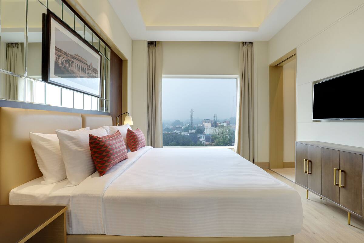 Quarto de hotel com uma cama grande, televisão, vista para a cidade e um quadro na parede.