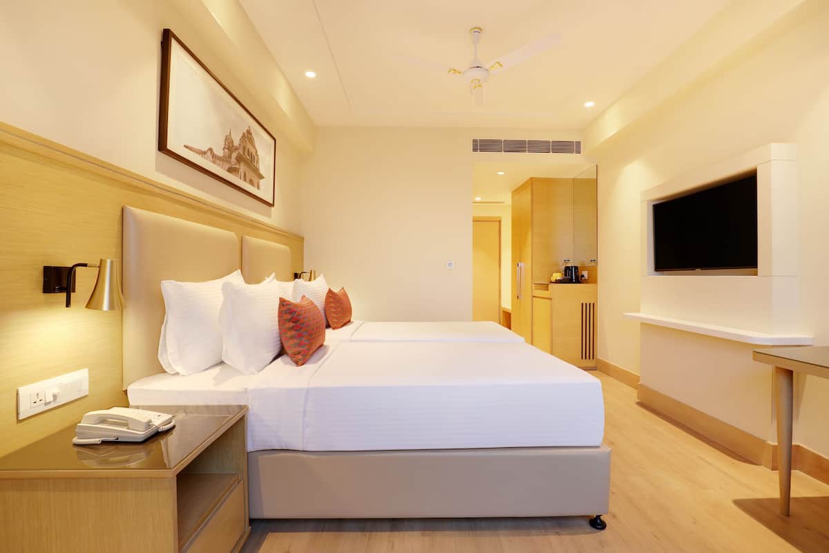 Quarto de hotel com cama grande, mesa de cabeceira e televisão em suporte.