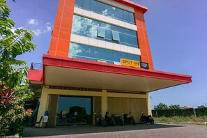 A multi-story building with a red and beige facade, a covered entrance, and several parked motorcycles. - Pondok Bintang (Somba Opu)