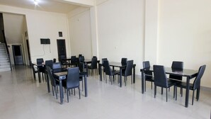 A spacious room with multiple tables and chairs, a flat-screen TV mounted on the wall, and a staircase leading to another area. - Pondok Bintang (Somba Opu)