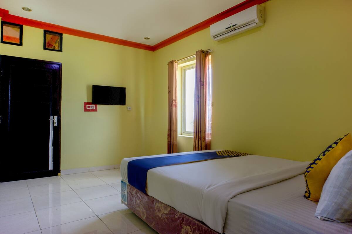 A hotel room with a bed, a television, a window with curtains, and a door.
