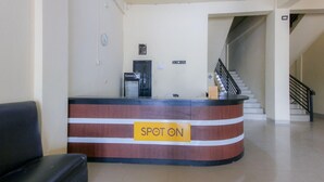 Una recepción con un letrero que dice 'SPOT ON', una máquina de café, un reloj y una escalera que sube a un nivel superior.