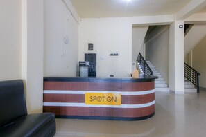 Ein Empfangsschalter mit einem Schild, auf dem 'SPOT ON' steht, eine Kaffeemaschine, eine Uhr und eine Treppe, die in einen oberen Bereich führt.