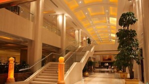 A spacious lobby with a grand staircase, marble flooring, and large potted plants.