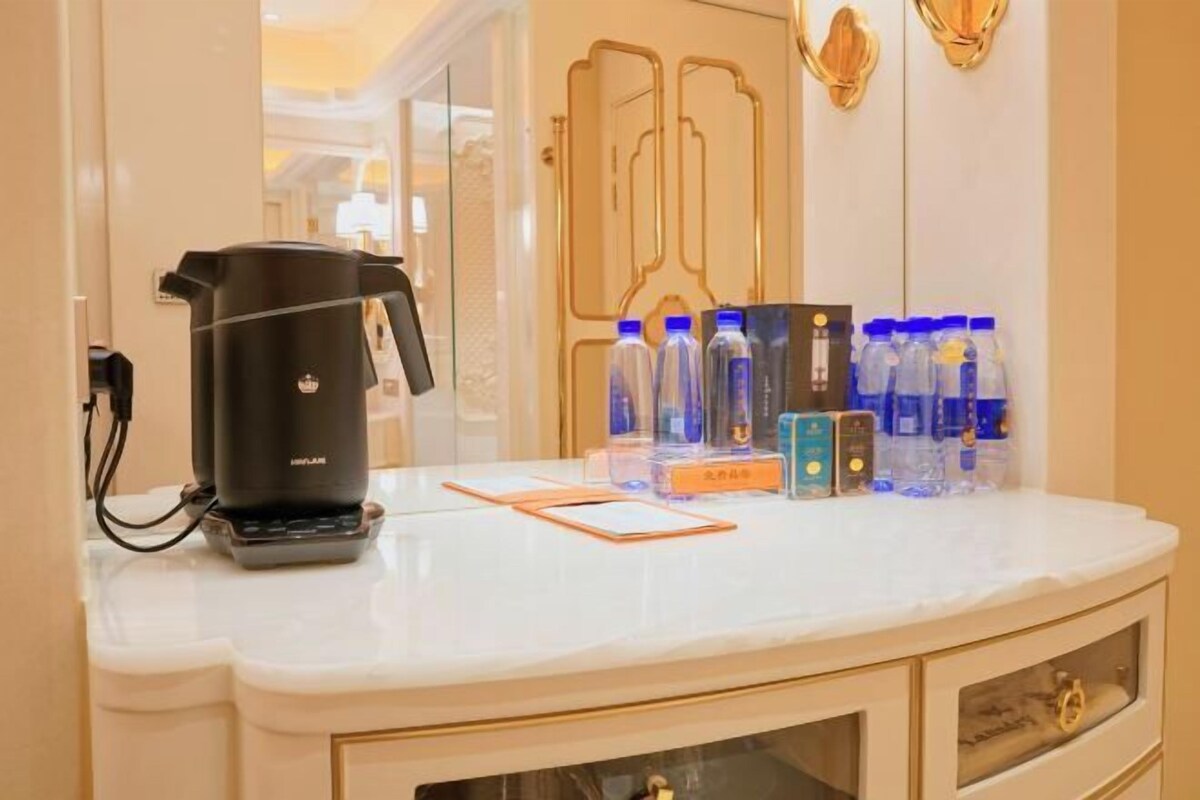 Habitación de hotel con encimera de mármol blanco, cafetera negra y varias botellas de agua.