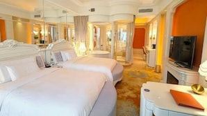 A hotel room with two beds, a TV, a desk, and a bathroom with a shower and mirror.