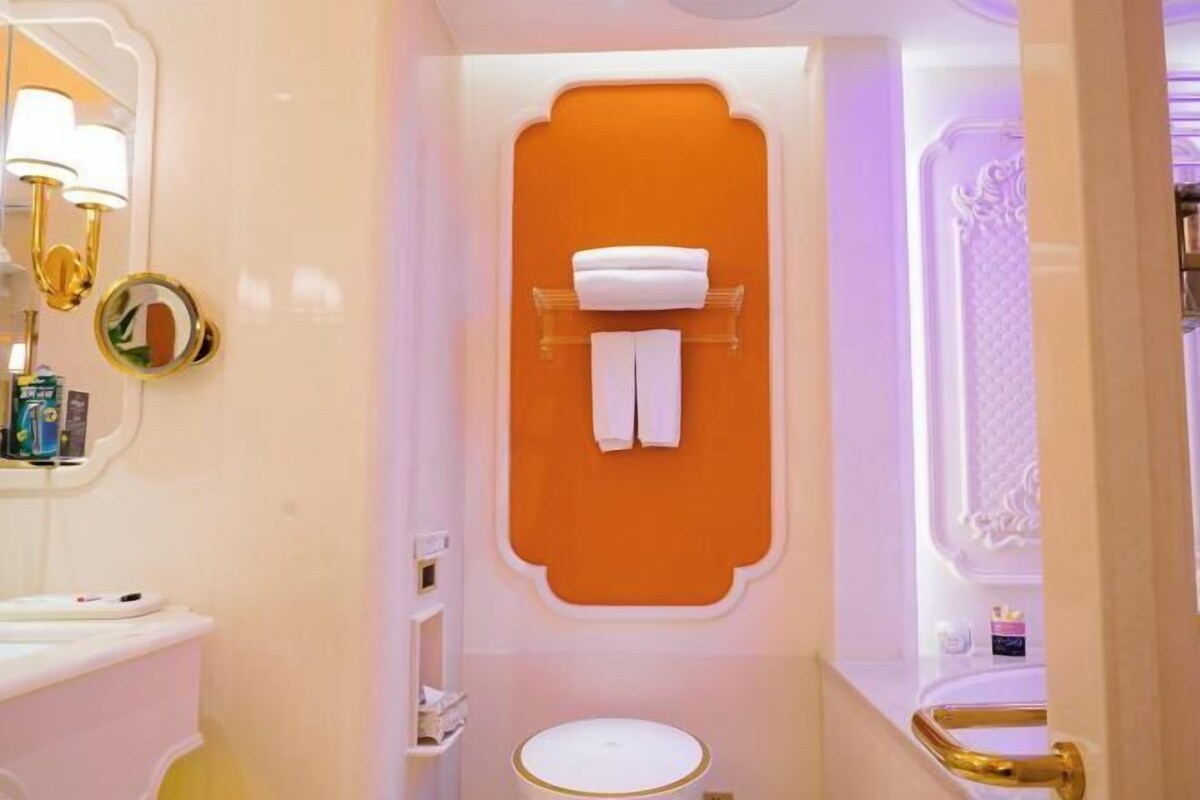 Un baño con un lavamanos blanco, un espejo con marco dorado y una pared de acento naranja.
