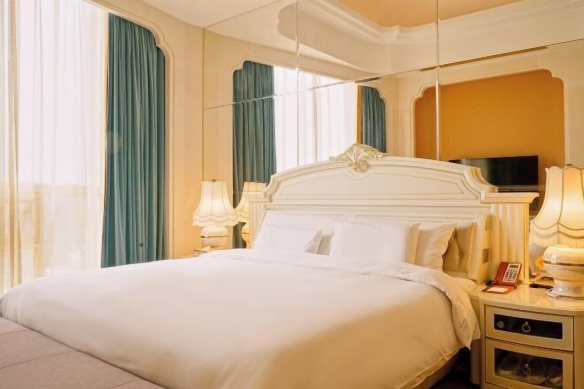 Una habitación de hotel con una cama grande, dos mesitas de noche con lámparas, un televisor y un espejo.