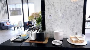 Un buffet per la colazione con macchina del caffè, tostapane, piatti e pane.
