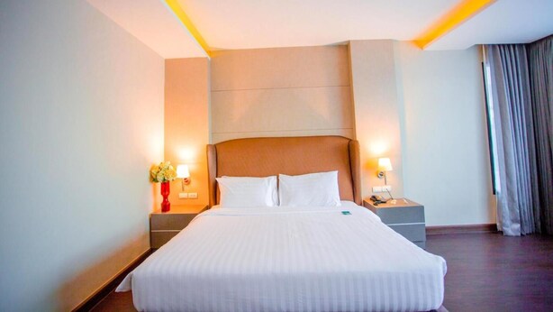 Una camera d'albergo con un letto grande, due comodini con lampade, un tavolino e un vaso con fiori.