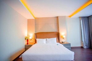 Een hotelkamer met een groot bed, twee nachtkastjes met lampen, een bijzettafeltje en een vaas met bloemen.