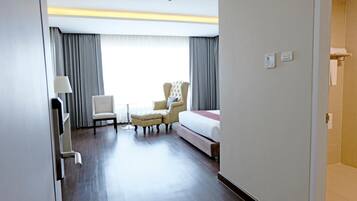 A hotel room with a bed, a chair, a small table, and a window with curtains.