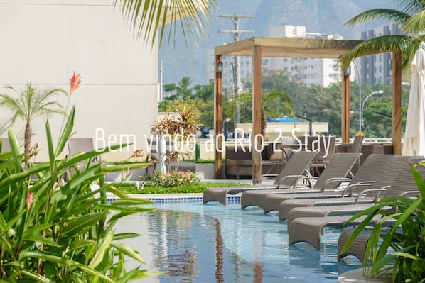 A rooftop pool area with lounge chairs and a pergola.