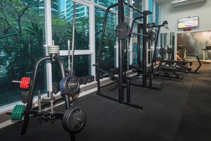 A gym with various exercise equipment, large windows, and a TV screen displaying a race.
