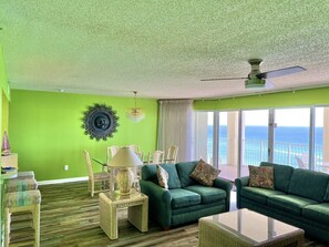 Una sala de estar con pared verde, ventilador de techo y vista al océano.