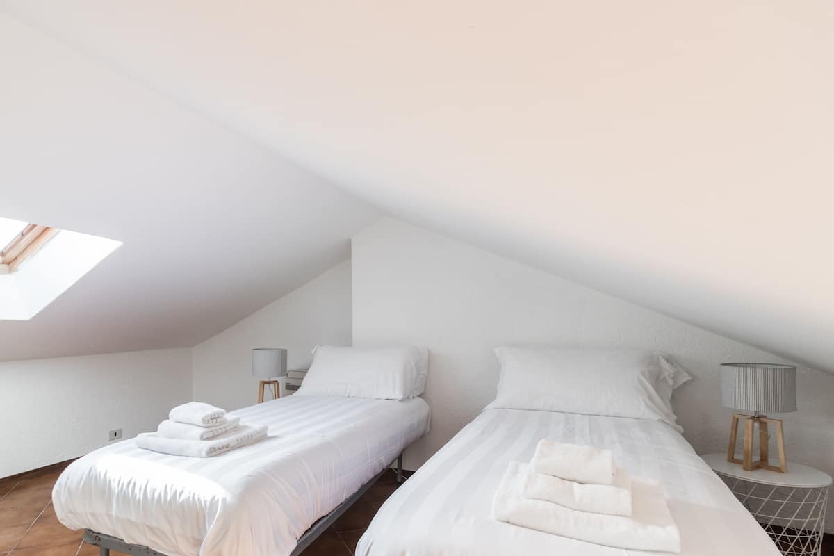 Una camera da letto con due letti, un lucernario e un piccolo tavolo con una lampada.