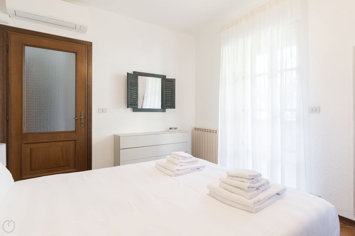 Una camera d'albergo con un letto, una cassettiera, uno specchio e una finestra con tende.