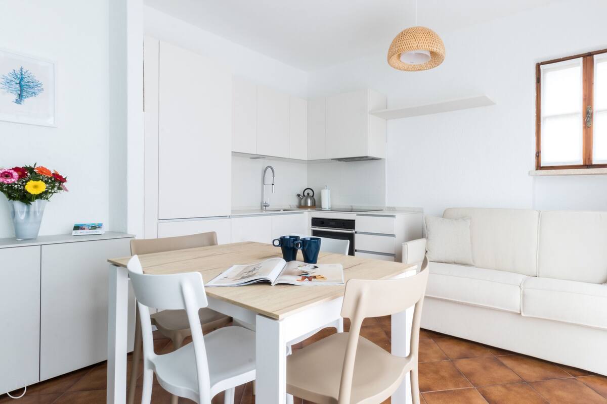 Un soggiorno e zona pranzo dal design moderno, in tonalità bianche, con divano, tavolo e sedie.