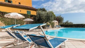 A poolside area with lounge chairs and umbrellas, a clear blue pool, and a building with a yellow facade. - Italianway - Il Borgo apartments (Finale Ligure)