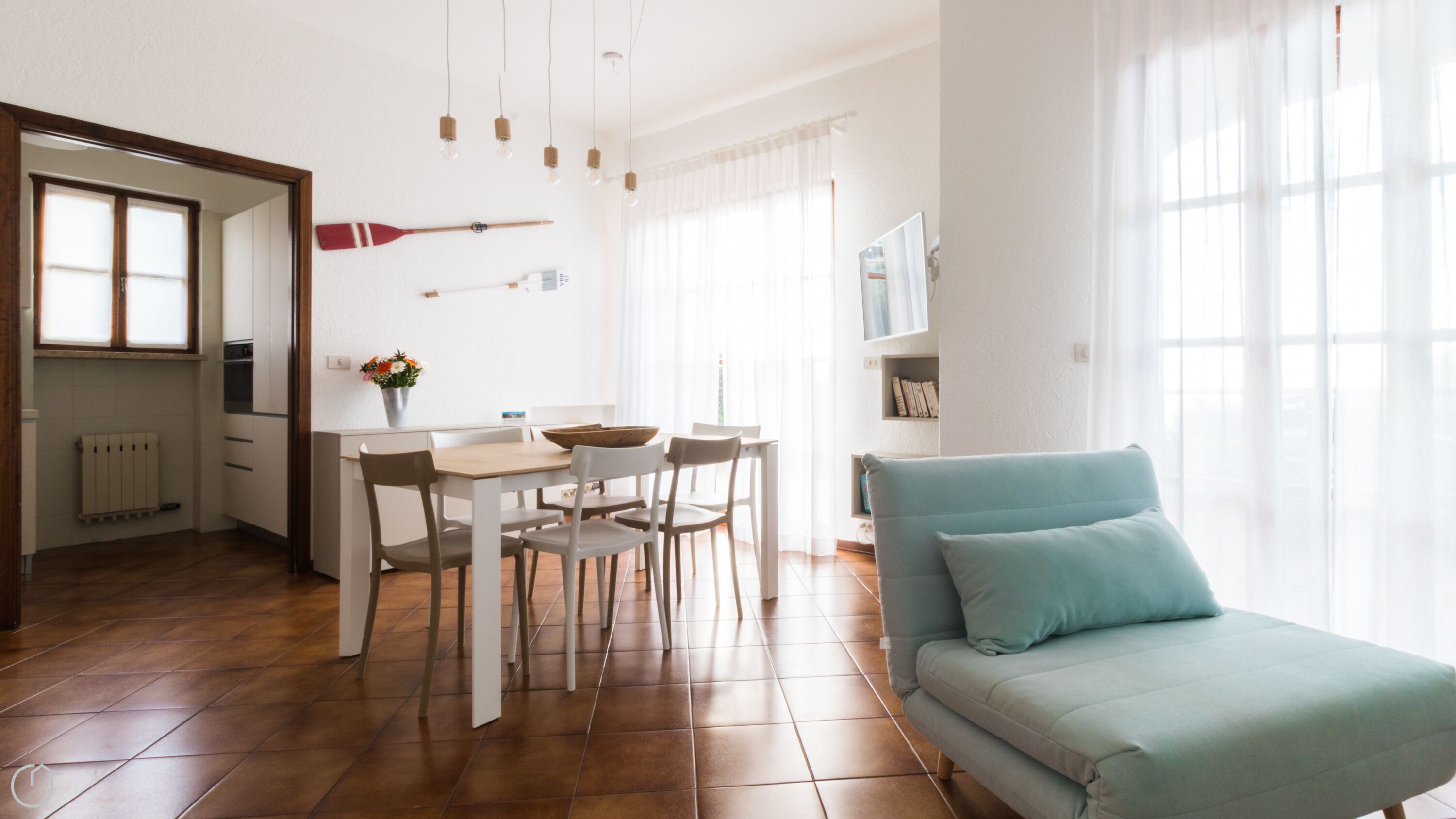 Une cuisine moderne avec des meubles blancs, une table à manger avec des chaises, un canapé bleu et une fenêtre ornée de rideaux légers.