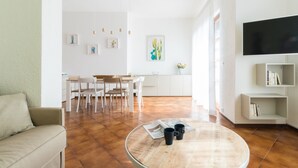 A modern living room with a round coffee table, a sofa, a dining area with chairs, a TV mounted on the wall, and a bookshelf. - Italianway - Il Borgo apartments (Finale Ligure)