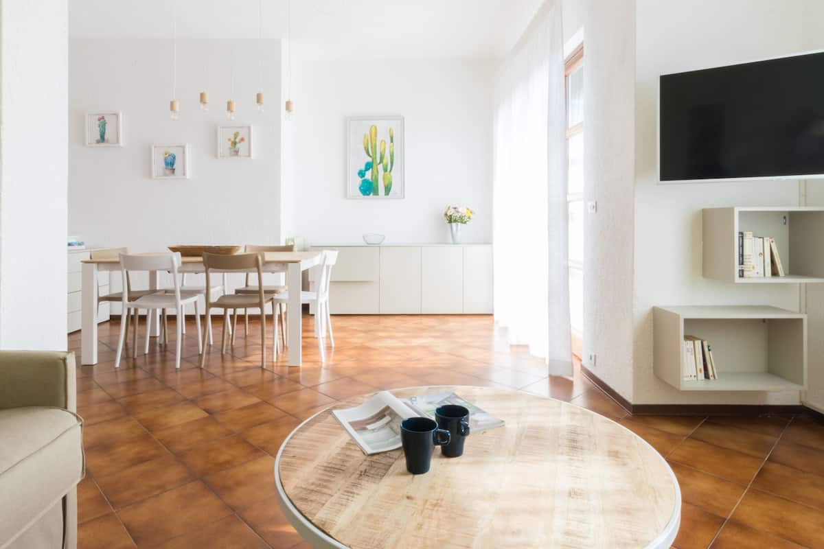 Un soggiorno moderno con un tavolino rotondo, un divano, un'area pranzo con sedie, una TV a parete e una libreria.
