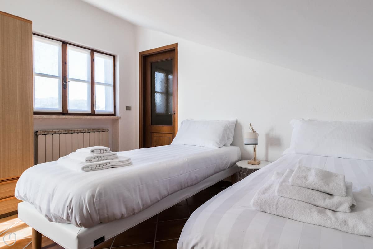 Camera d'albergo con due letti, una porta in legno, una finestra e un comodino con una lampada.