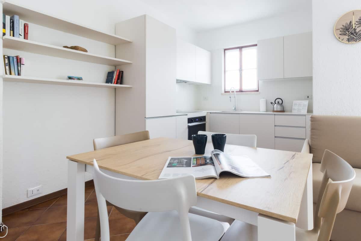 Una cucina moderna e minimalista con mobili bianchi, un tavolo da pranzo con sedie e una piccola finestra.
