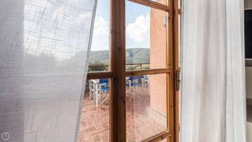 A room with a large window, a wooden door, and a view of an outdoor patio with tables and chairs.