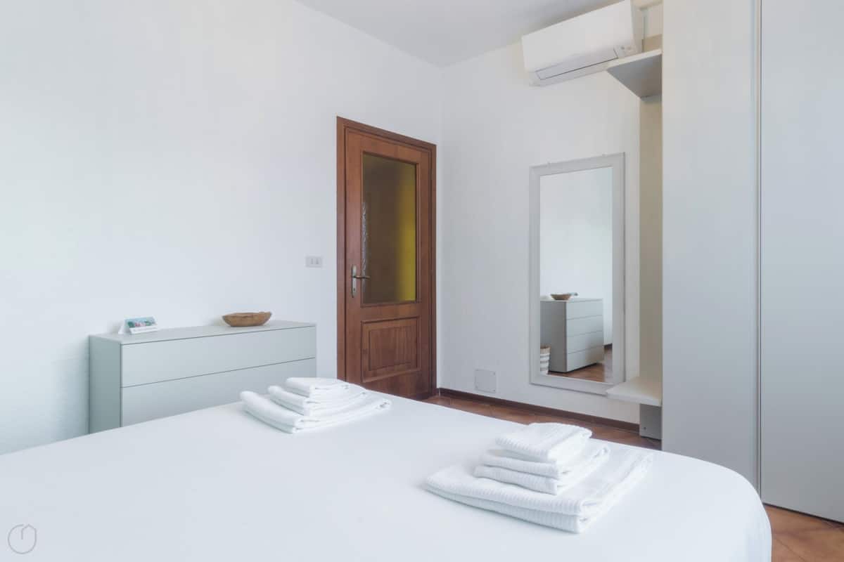 Una camera d'albergo con un letto, una cassettiera, una porta in legno, uno specchio e un armadio.