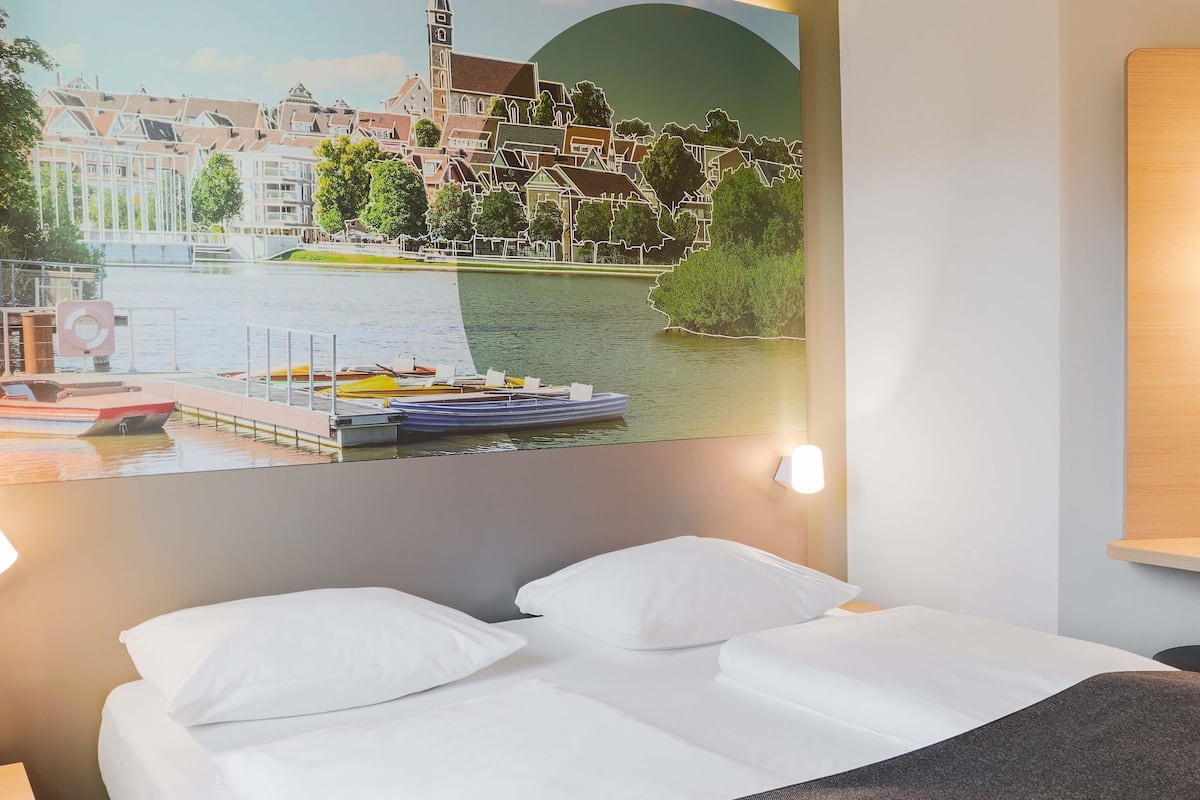 A hotel room with a bed, a nightstand, and a wall-mounted light.