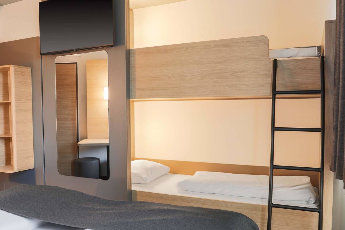 A modern hotel room with bunk beds, a desk, and a mirror.
