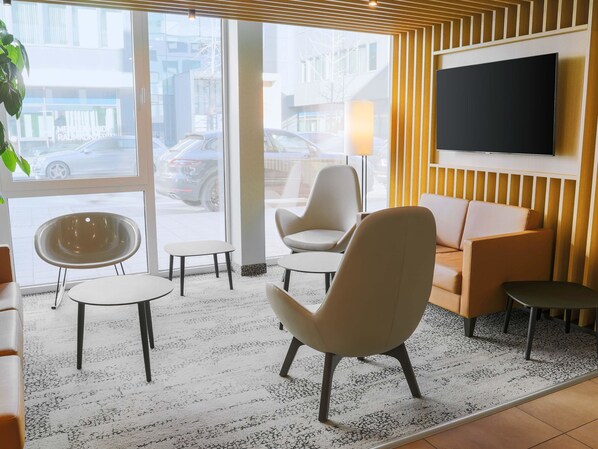 A modern hotel lobby with a large TV, comfortable seating, and a view of the street outside.