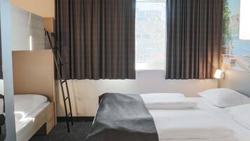 Una habitación de hotel con cama, escritorio, silla y ventana con cortinas.