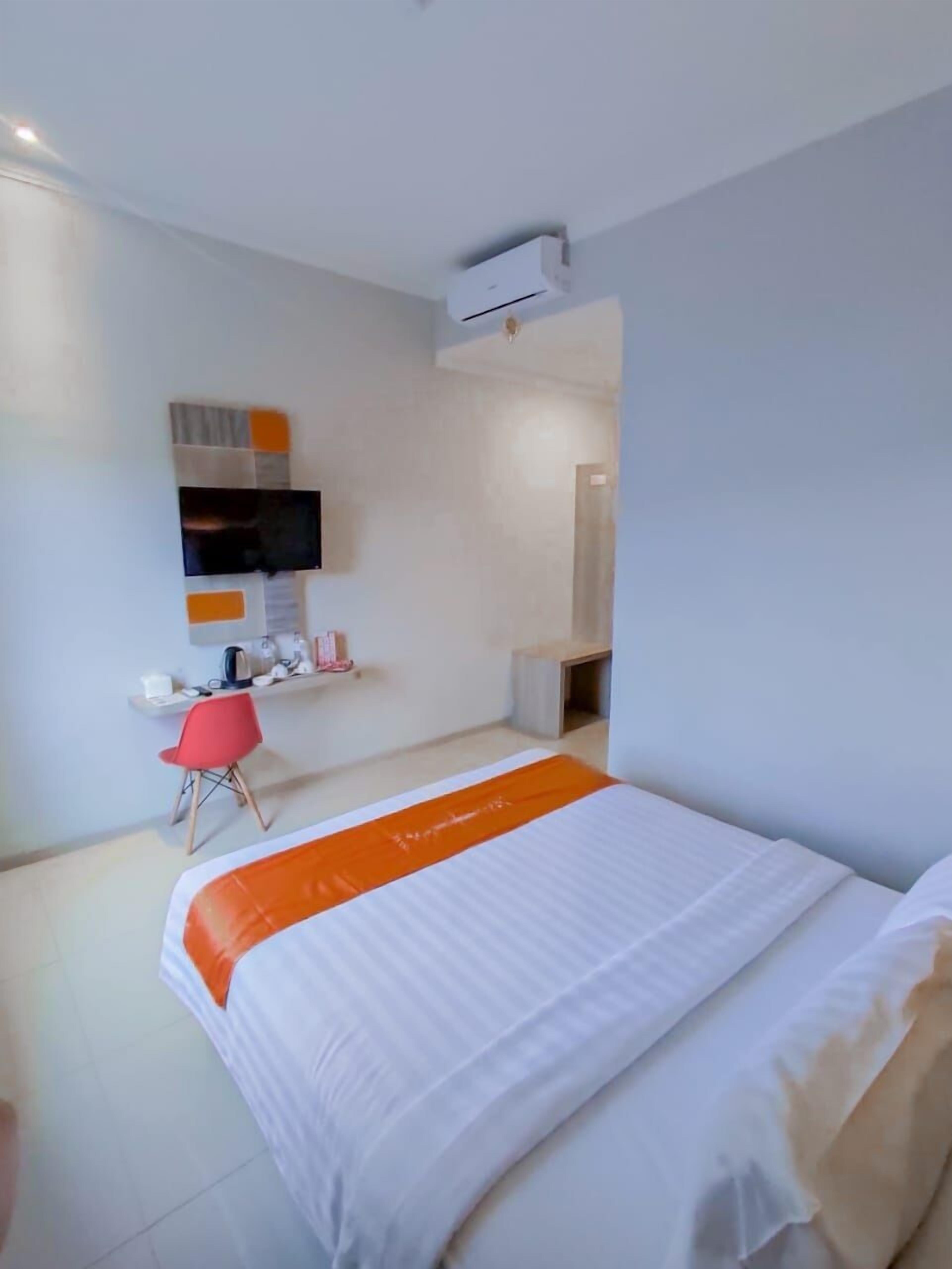 Habitación de hotel con cama, escritorio, silla y televisor montado en la pared.